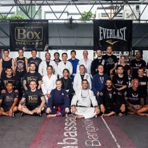 Un grand groupe de personnes en tenue de sport et kimonos d'arts martiaux posant pour une photo de groupe dans une salle de boxe.