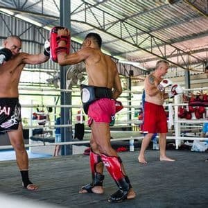 Des hommes d'un voyage de groupe WeRoad lors d'une leçon de Muay Thai, s'entraînant aux coups de poing avec des entraîneurs sur un ring de boxe.