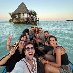 Un gruppo WeRoad si scatta un selfie su una barca con un edificio su uno scoglio sullo sfondo.
