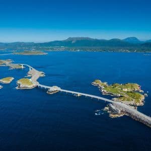Vue aérienne d'une route côtière sinueuse qui relie plusieurs petites îles rocheuses dans une mer d'un bleu profond sous un ciel clair.