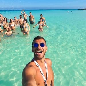 Un hombre se toma una selfie con un grupo de viaje de WeRoad mientras posan juntos en el mar turquesa claro en un día soleado.