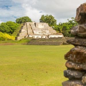 Une grande pyramide de pierre à degrés se dresse dans une clairière verdoyante, entourée d'arbres luxuriants sous un ciel nuageux.