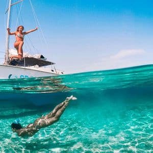 Una toma doble de un viaje en grupo de WeRoad, con una mujer en un velero y otra nadando bajo el agua en aguas claras y turquesas.