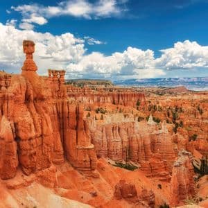 Un ampio canyon pieno di alte guglie di arenaria arancione, note come hoodoos, sotto un cielo blu con nuvole bianche.