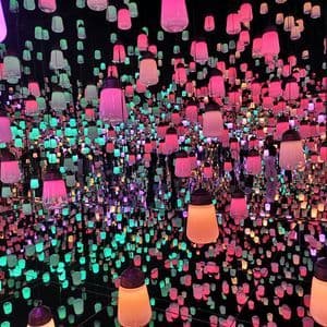 Una habitación llena de cientos de farolillos colgantes que brillan en tonos rosa y aguamarina, reflejados infinitamente por paredes con espejos.