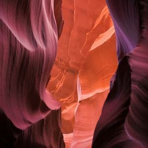 A close-up view of the smooth, wavy walls of a slot canyon, showing layers of purple and orange rock.