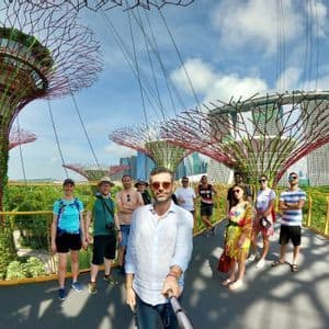 Un viaje en grupo de WeRoad se toma una selfie en una pasarela elevada entre grandes estructuras arbóreas futuristas con un paisaje urbano de fondo.
