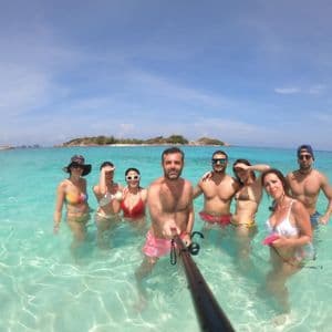 Un grupo de WeRoad se toma una selfie con un palo selfie en aguas claras, poco profundas y turquesas, con islas de fondo.