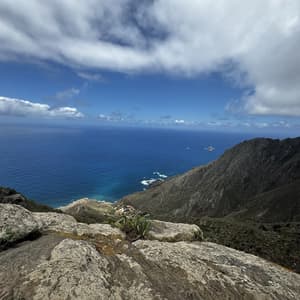 Vista da una scogliera rocciosa di una costa montuosa che si affaccia sull'oceano blu sotto un cielo parzialmente nuvoloso.