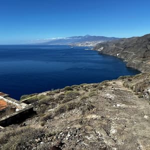 Una vista da una scogliera su un oceano blu intenso verso una costa vulcanica con una città e una montagna in lontananza.