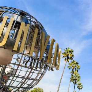 Un'inquadratura dal basso della scultura del globo degli Universal Studios con alte palme sullo sfondo di un cielo blu.