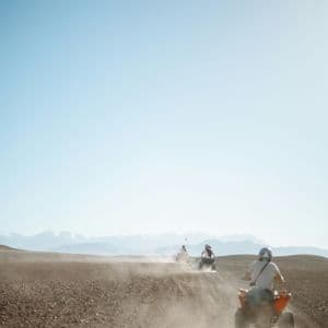 Un viaggio di gruppo WeRoad in quad su un sentiero polveroso nel deserto, con le montagne visibili in lontananza.