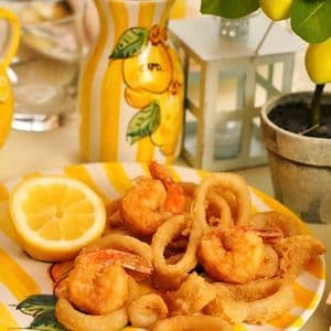 Un plato de calamares y camarones fritos con una rodaja de limón en un plato de rayas amarillas y blancas.