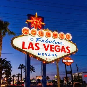 Das 'Welcome to Fabulous Las Vegas'-Schild, von Neonlichtern vor einem Dämmerungshimmel mit Palmen beleuchtet.