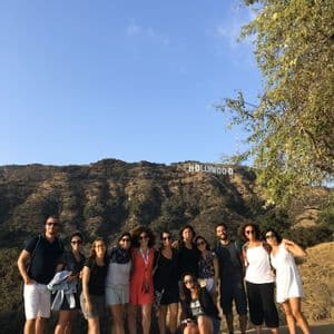 A WeRoad group trip poses for a photo on a hill with the Hollywood sign in the background on a sunny day.