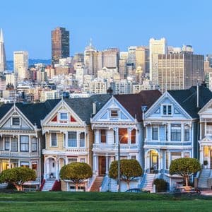 Une rangée de maisons victoriennes colorées se dresse devant un panorama urbain moderne au crépuscule.