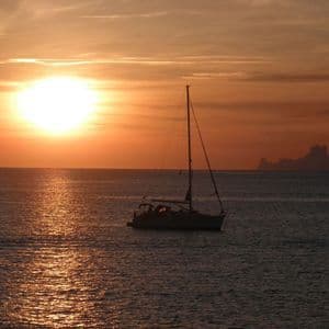 Un viaje en grupo de WeRoad en velero durante un atardecer dorado, con el sol reflejándose en el agua.