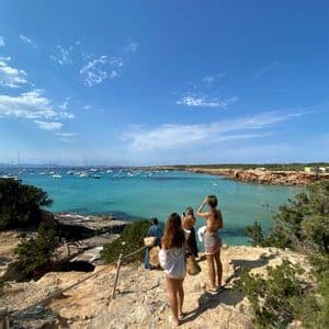 Un viaje en grupo WeRoad de mujeres en un acantilado rocoso con vistas a una bahía turquesa llena de veleros.