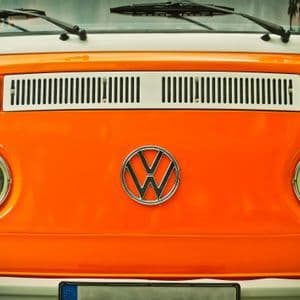 Primer plano del frontal de una furgoneta Volkswagen vintage naranja y blanca, mostrando su icónico logo y faros redondos.