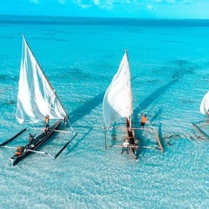 Vue aérienne d'un voyage de groupe WeRoad naviguant sur trois pirogues traditionnelles à balancier sur des eaux peu profondes et turquoises.