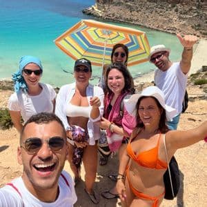 Un gruppo WeRoad scatta un selfie sorridente su una scogliera a picco su una spiaggia con acqua turchese.