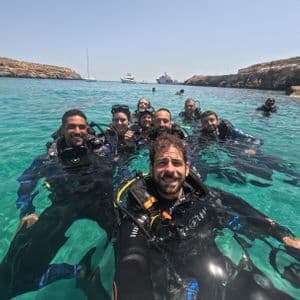 Un viaggio di gruppo WeRoad con persone sorridenti in attrezzatura subacquea completa che si fanno un selfie mentre galleggiano in acqua cristallina turchese.