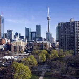 A sprawling city skyline with a prominent needle tower and skyscrapers, seen over a green park under a clear blue sky.