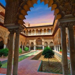 Un cortile moresco ornato con un giardino centrale, una lunga piscina stretta e archi finemente intagliati visti al tramonto.