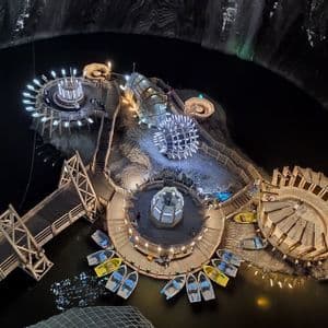 Un parco divertimenti illuminato costruito su un'isola di legno all'interno di una vasta caverna sotterranea con un lago e barche a remi.