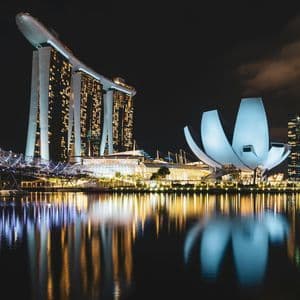 Eine moderne Stadtskyline bei Nacht, mit beleuchteten Wolkenkratzern und einem lotusförmigen Gebäude, das sich im Wasser spiegelt.