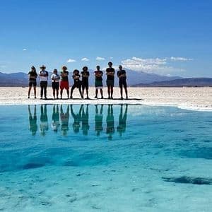 Un viaje en grupo de WeRoad se refleja en una piscina turquesa en un vasto salar bajo un cielo azul claro.