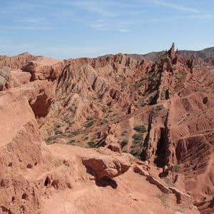 Une vue imprenable sur un canyon avec des formations rocheuses rouges érodées et une végétation clairsemée sous un ciel bleu pâle.