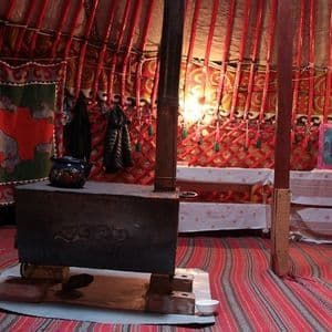 L'intérieur d'une yourte traditionnelle avec un poêle à bois central, une théière bleue et des textiles à motifs rouges recouvrant les murs et le sol.