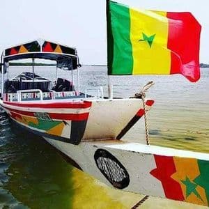 Ein farbenfrohes Boot mit der senegalesischen Flagge am Bug schwimmt in ruhigem Wasser.