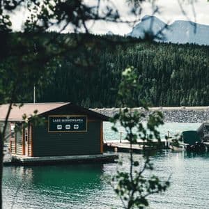 Un hangar à bateaux sur le lac Minnewanka avec un quai et des bateaux, encadré par des arbres avec une montagne et une forêt en arrière-plan.