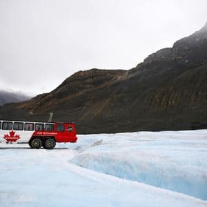 Un voyage de groupe WeRoad à bord d'un bus Ice Explorer rouge et blanc garé sur un vaste glacier au pied de montagnes rocheuses.