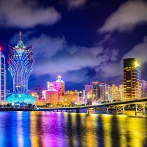 Panorama urbain nocturne avec néons colorés se reflétant sur l'eau, et un pont.
