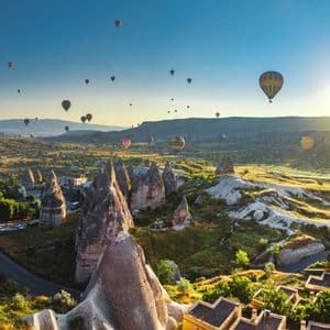 Decenas de globos aerostáticos flotan sobre un valle con formaciones rocosas únicas y un pueblo al amanecer.