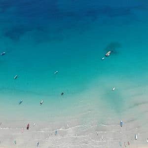 Luftaufnahme von vielen kleinen Booten, die auf einem weißen Sandstrand und im klaren türkisfarbenen Meer verstreut sind.