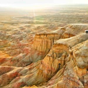 Vista aerea di un SUV parcheggiato su una scogliera che si affaccia su un paesaggio desertico di canyon erosi e colorati all'alba.