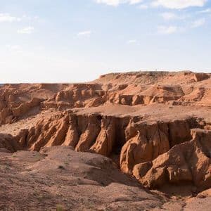 Una persona solitaria si trova sul bordo di un vasto canyon di roccia rossa sotto un cielo azzurro pallido con nuvole leggere.