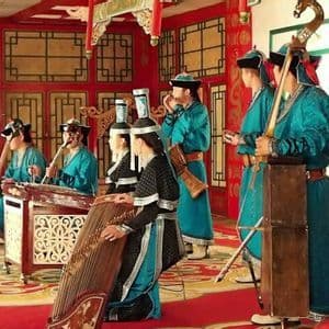 Un gruppo di musicisti in colorati costumi tradizionali che suonano vari strumenti a corda e a percussione su un palco rosso ornato.