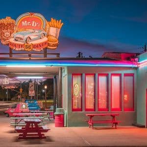 The exterior of Mr. D'z, a retro Route 66 diner, glows with colorful neon signs at twilight.