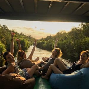 Un viaje en grupo de WeRoad de mujeres relajándose en pufs en un barco navegando por un río selvático al atardecer.