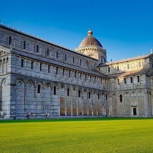 La Cattedrale di Pisa e la Torre Pendente di Pisa si ergono su un ampio prato verde sotto un cielo azzurro limpido.