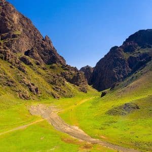 Un viaggio di gruppo WeRoad percorre un sentiero in un'ampia valle verde tra montagne rocciose, sotto un cielo azzurro limpido.