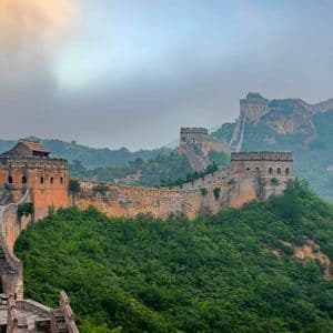 Un mur de pierre historique avec des tours de guet serpente à travers des montagnes verdoyantes sous un ciel brumeux.