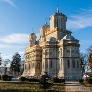 Eine prächtige, helle Kathedrale mit mehreren Kuppeln und Türmen steht in einem grünen Park unter einem klaren blauen Himmel.