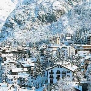 Un villaggio innevato con chalet e pini si trova ai piedi di una grande montagna.