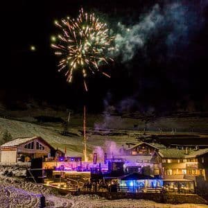 I fuochi d'artificio illuminano il cielo notturno sopra una località di montagna innevata dove un gruppo WeRoad festeggia.